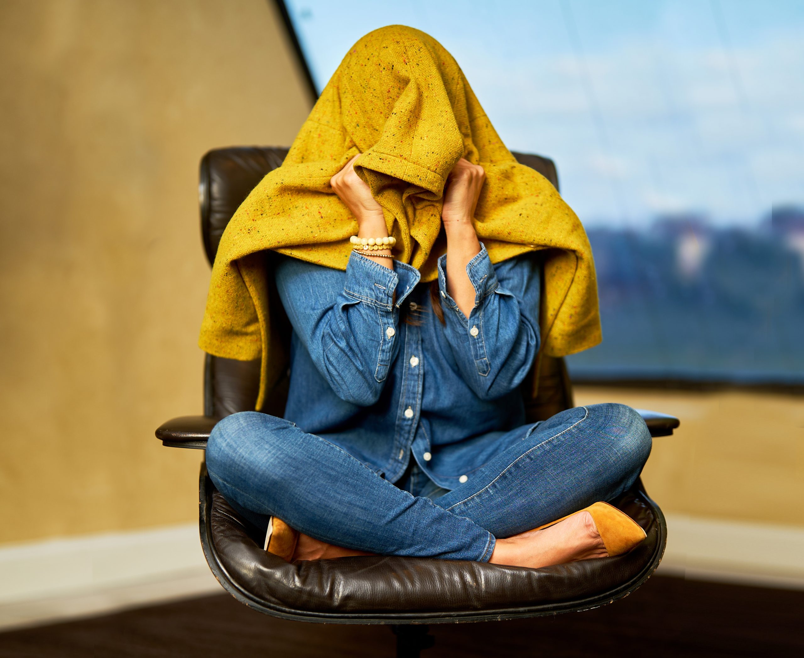 Woman sitting in chair with coat over head.